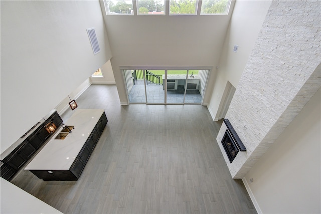 unfurnished living room featuring light wood-type flooring, a wealth of natural light, a towering ceiling, and a stone fireplace