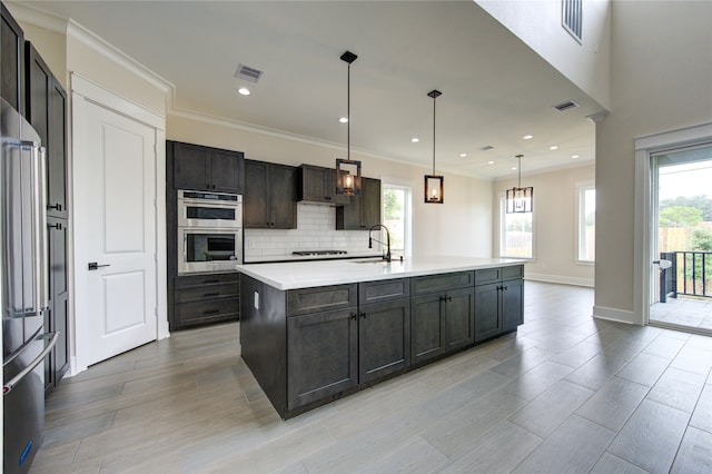 kitchen with light wood-type flooring, stainless steel appliances, an island with sink, and hanging light fixtures