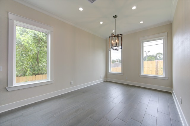 spare room with wood-type flooring, ornamental molding, a chandelier, and a healthy amount of sunlight