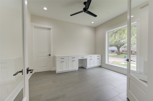 unfurnished office with built in desk, a healthy amount of sunlight, ceiling fan, and light hardwood / wood-style floors