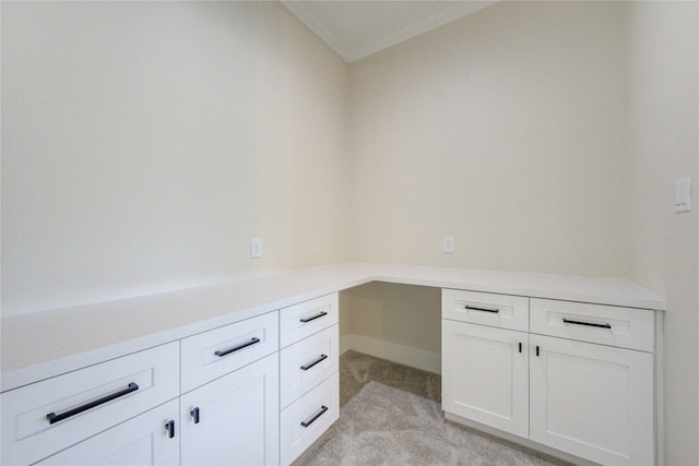 unfurnished office featuring light carpet, crown molding, and built in desk