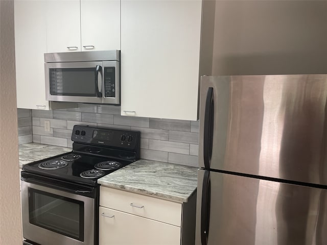 kitchen featuring appliances with stainless steel finishes, white cabinetry, light stone counters, and tasteful backsplash