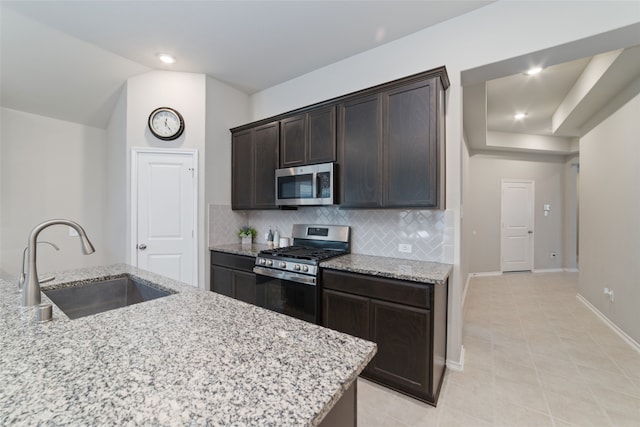 kitchen with light stone countertops, tasteful backsplash, stainless steel appliances, sink, and dark brown cabinetry