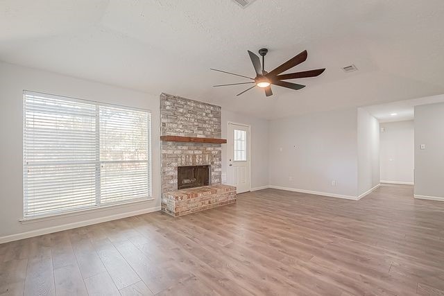 unfurnished living room featuring ceiling fan, a fireplace, wood-type flooring, and vaulted ceiling