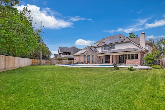 rear view of property featuring a fenced in pool, a yard, solar panels, and a patio area