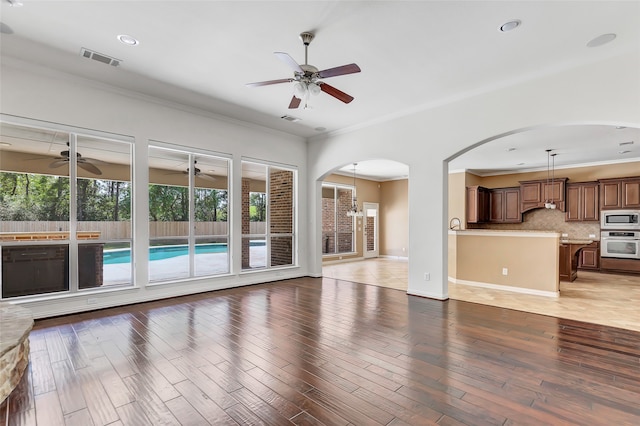 unfurnished living room featuring ceiling fan, wood-type flooring, and ornamental molding