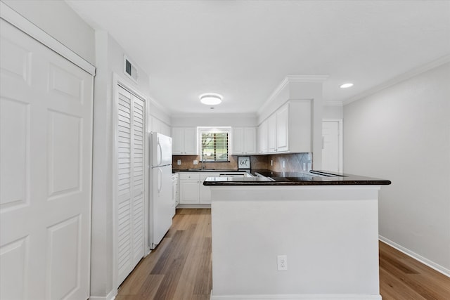 kitchen featuring light wood-type flooring, white refrigerator, backsplash, white cabinets, and kitchen peninsula