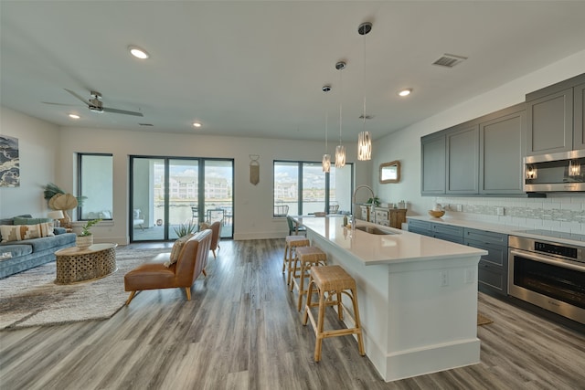 kitchen with hardwood / wood-style floors, appliances with stainless steel finishes, sink, ceiling fan, and a center island with sink