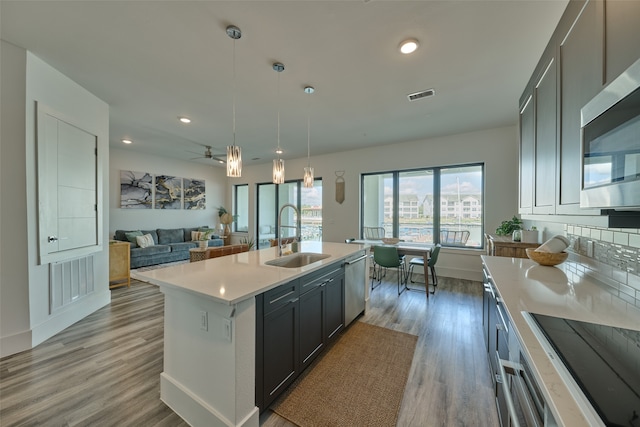 kitchen featuring a kitchen island with sink, stainless steel appliances, decorative light fixtures, sink, and light hardwood / wood-style floors