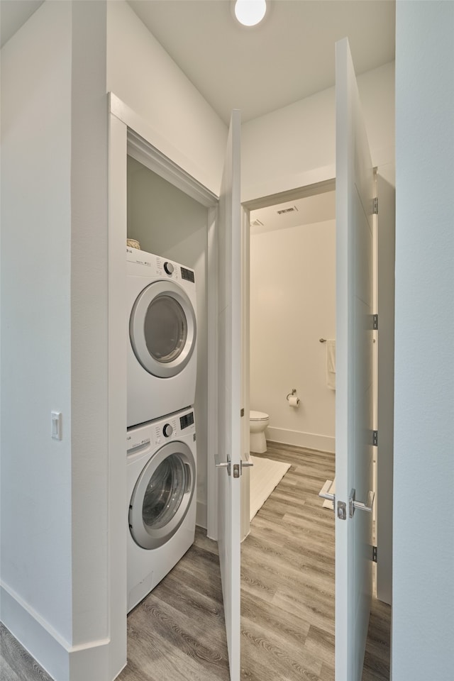 clothes washing area featuring wood-type flooring and stacked washer / drying machine