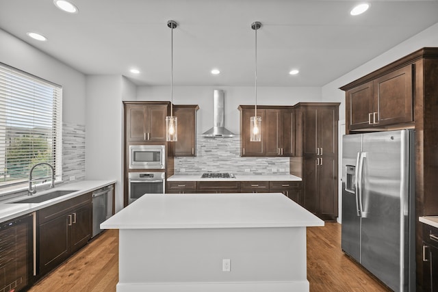 kitchen featuring appliances with stainless steel finishes, hanging light fixtures, a center island, and wall chimney range hood