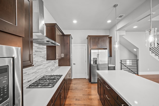 kitchen featuring appliances with stainless steel finishes, pendant lighting, wall chimney range hood, and light hardwood / wood-style flooring