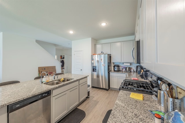 kitchen with light stone counters, light hardwood / wood-style floors, appliances with stainless steel finishes, and sink