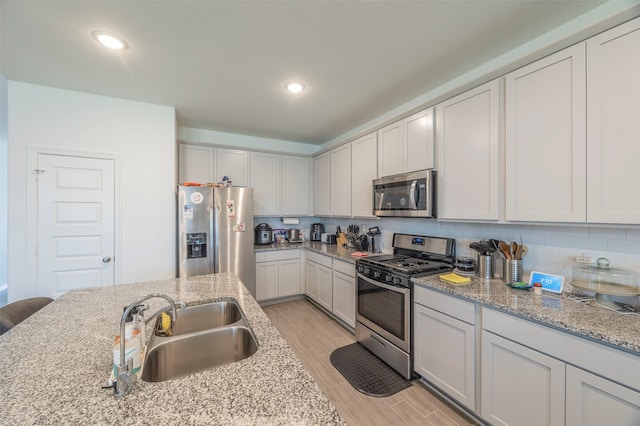 kitchen featuring light stone counters, white cabinets, sink, appliances with stainless steel finishes, and light wood-type flooring