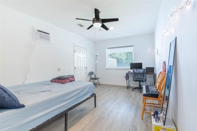 bedroom with ceiling fan, an AC wall unit, and light hardwood / wood-style flooring