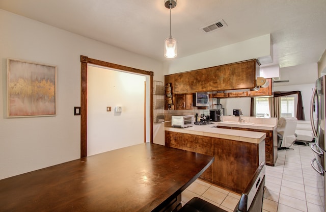 kitchen with kitchen peninsula, hanging light fixtures, light tile patterned floors, and sink