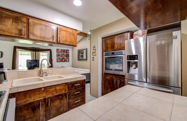 kitchen featuring tile countertops, sink, light tile patterned flooring, and stainless steel appliances