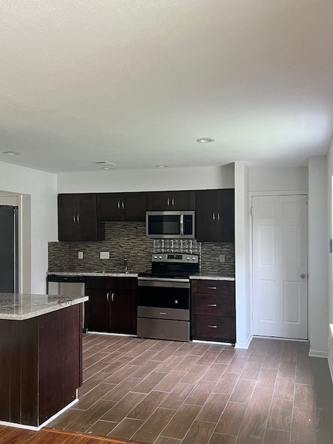 kitchen featuring appliances with stainless steel finishes, tasteful backsplash, wood-type flooring, and dark brown cabinetry