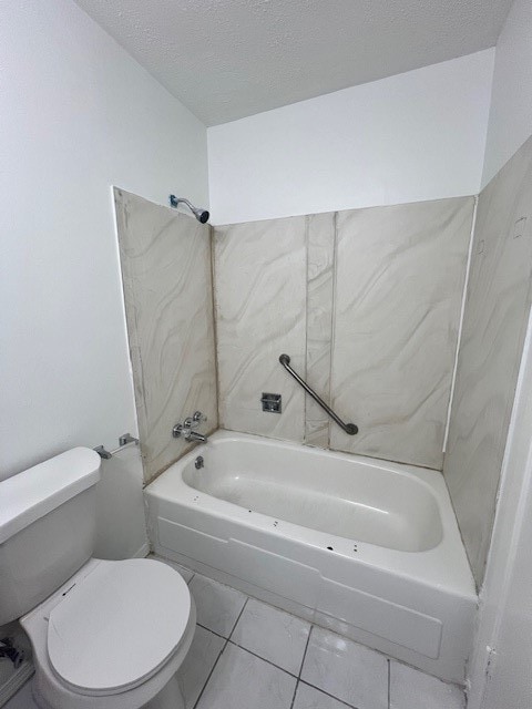 bathroom with a textured ceiling, toilet, tile patterned floors, and washtub / shower combination