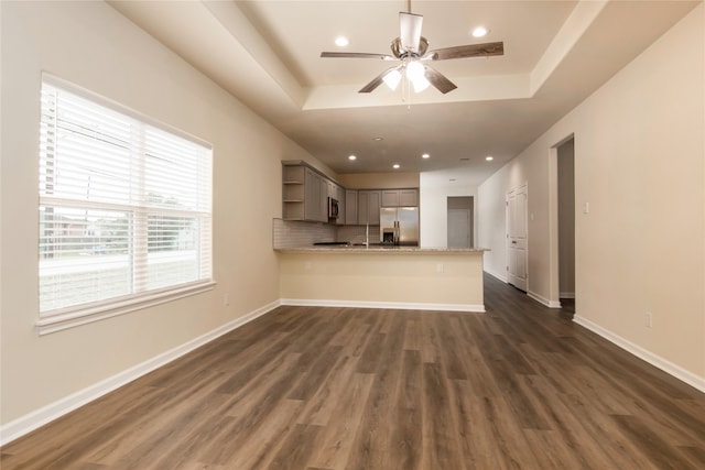 unfurnished living room featuring a raised ceiling, ceiling fan, and dark hardwood / wood-style flooring