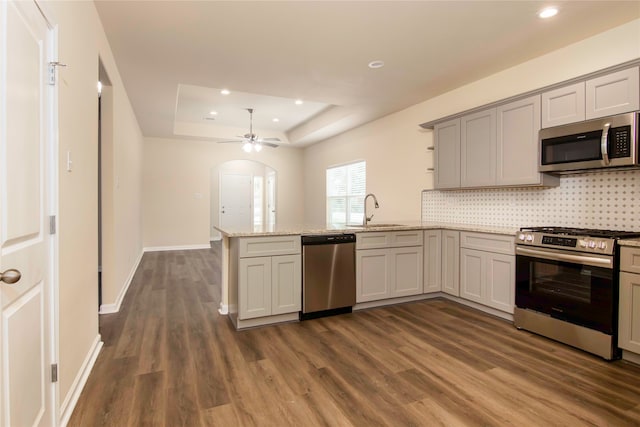 kitchen featuring stainless steel appliances, dark hardwood / wood-style flooring, kitchen peninsula, sink, and a tray ceiling