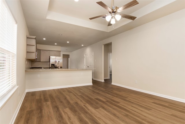 unfurnished living room with a raised ceiling, dark hardwood / wood-style flooring, and ceiling fan