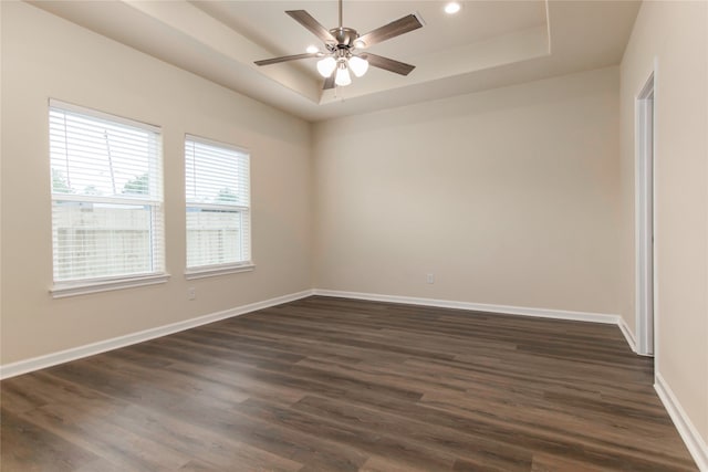 empty room featuring a raised ceiling, ceiling fan, and dark hardwood / wood-style flooring