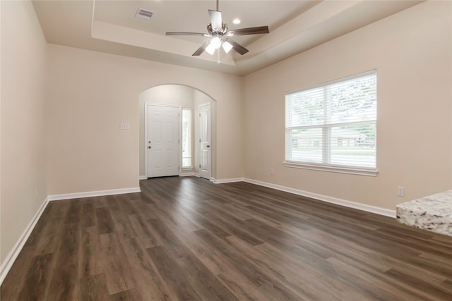 unfurnished room with ceiling fan, dark hardwood / wood-style floors, and a tray ceiling