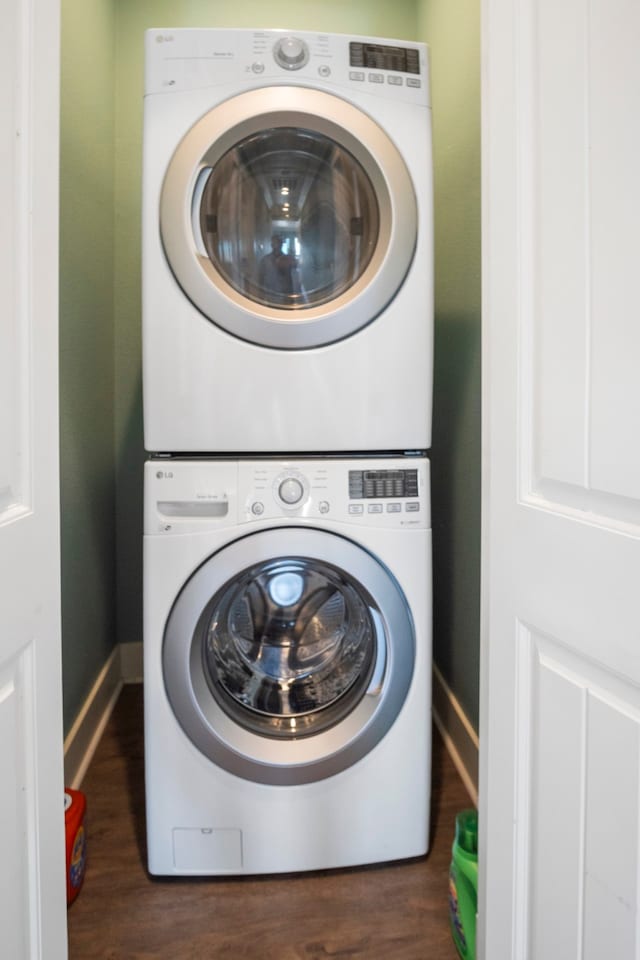 laundry area with dark hardwood / wood-style floors and stacked washing maching and dryer