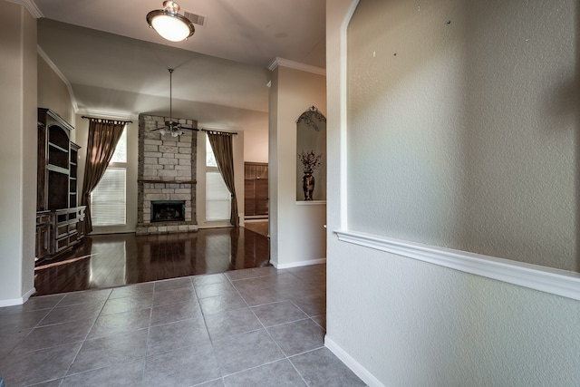 unfurnished living room with ceiling fan, a stone fireplace, wood-type flooring, and ornamental molding