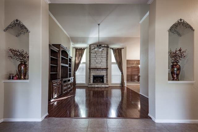 unfurnished living room with hardwood / wood-style floors, ceiling fan, a stone fireplace, and ornamental molding