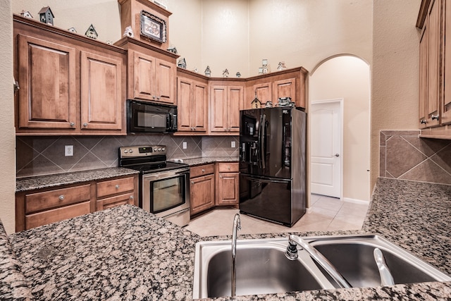 kitchen with sink, tasteful backsplash, dark stone counters, light tile patterned flooring, and black appliances