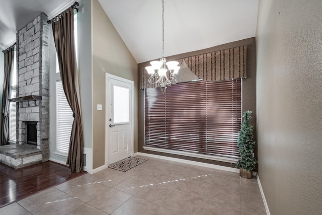 foyer entrance featuring a notable chandelier, light tile patterned floors, a fireplace, and vaulted ceiling