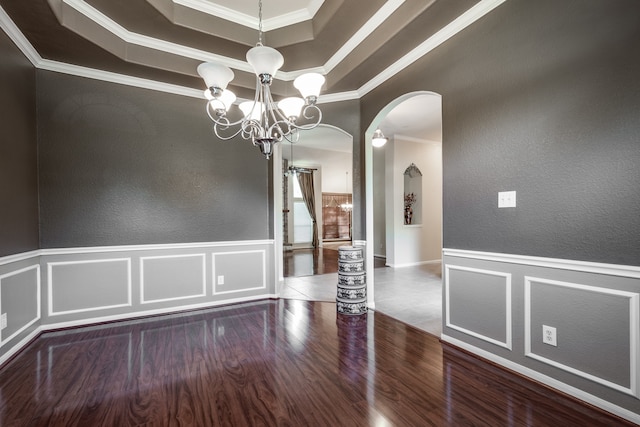 empty room featuring wood-type flooring, crown molding, a tray ceiling, and a chandelier