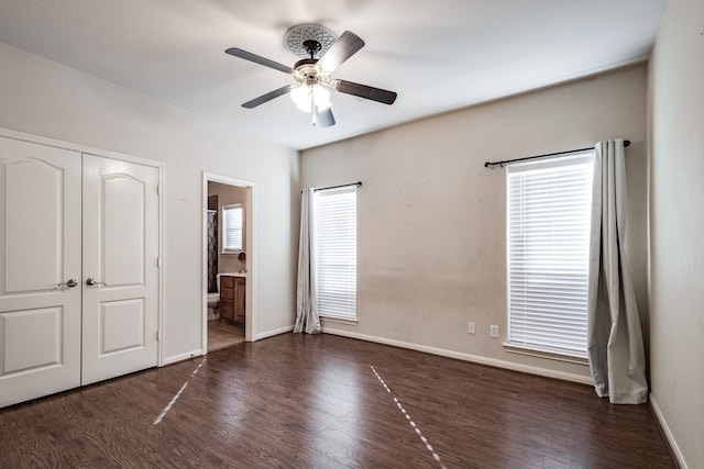 unfurnished bedroom featuring a closet, ensuite bathroom, ceiling fan, and dark wood-type flooring