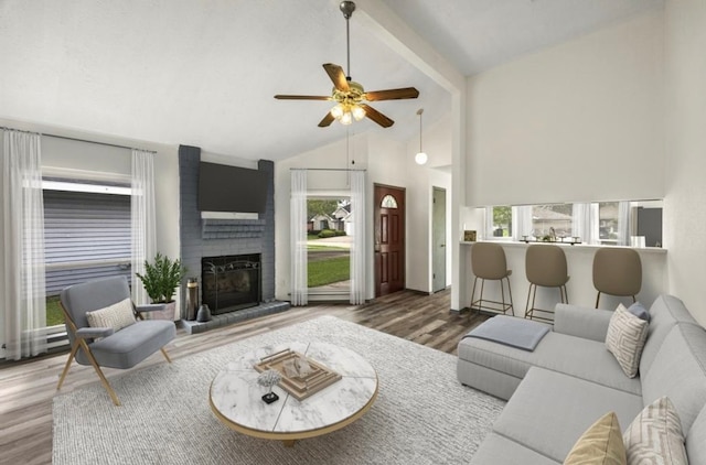 living room with a brick fireplace, hardwood / wood-style flooring, high vaulted ceiling, and ceiling fan