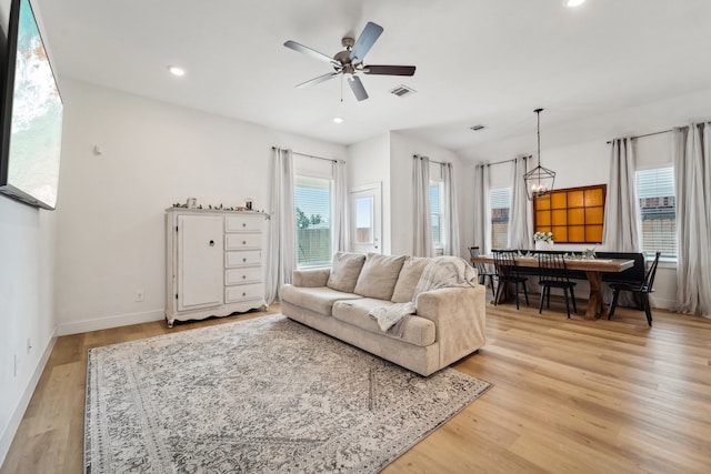 living room with ceiling fan with notable chandelier and light hardwood / wood-style flooring