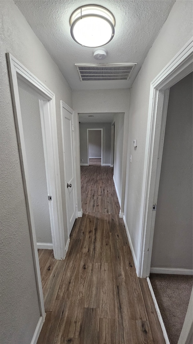 hall with a textured ceiling and dark hardwood / wood-style floors