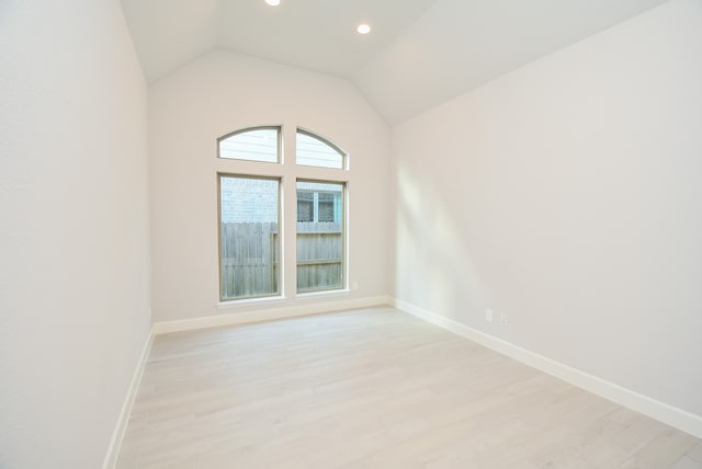 spare room featuring light wood-type flooring and vaulted ceiling