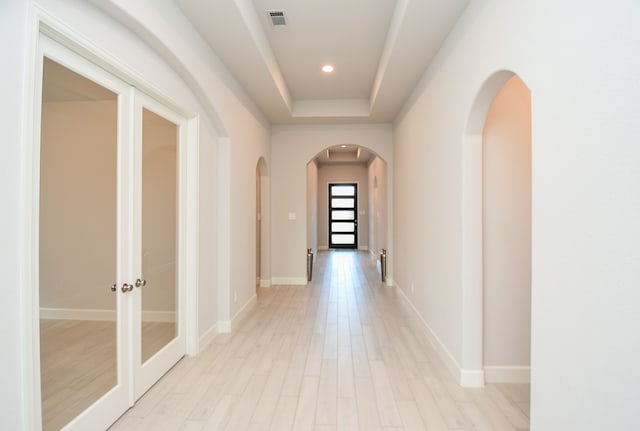 hallway featuring a tray ceiling, french doors, and light hardwood / wood-style floors