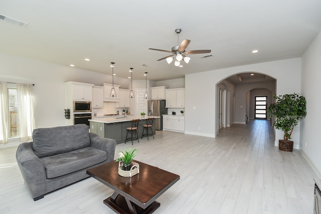 living room with a wealth of natural light, ceiling fan, sink, and light wood-type flooring