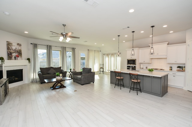 living room with ceiling fan, a tiled fireplace, sink, and light hardwood / wood-style floors