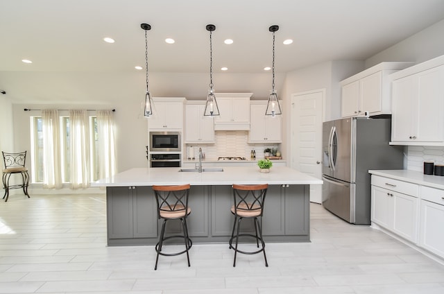 kitchen with white cabinets, appliances with stainless steel finishes, a kitchen island with sink, and sink