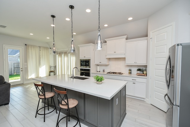 kitchen featuring pendant lighting, light hardwood / wood-style floors, a kitchen island with sink, stainless steel appliances, and white cabinetry