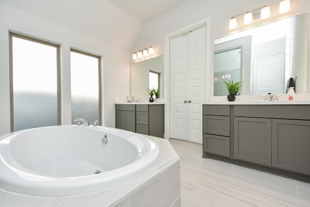 bathroom with vanity, lofted ceiling, and tiled bath