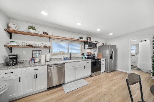 kitchen with white cabinetry, light stone counters, sink, appliances with stainless steel finishes, and light hardwood / wood-style floors