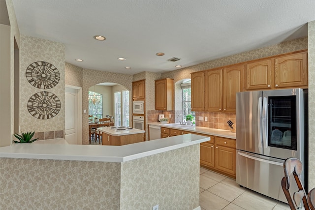 kitchen featuring white appliances, wallpapered walls, arched walkways, a center island, and light countertops