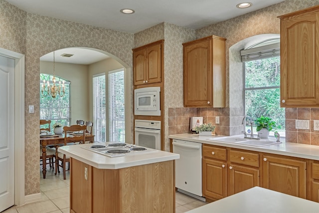 kitchen featuring white appliances, wallpapered walls, a center island, light countertops, and a sink