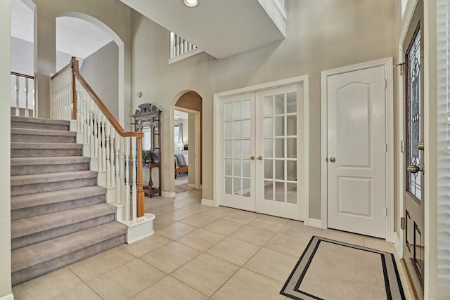 entryway featuring a towering ceiling, light tile patterned floors, baseboards, and french doors