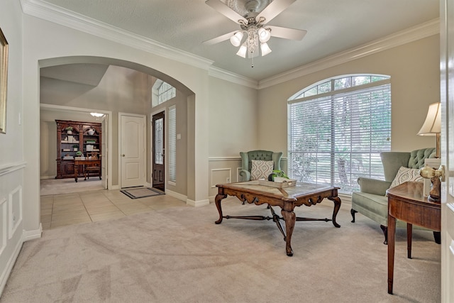 living area featuring arched walkways, light colored carpet, ornamental molding, light tile patterned flooring, and ceiling fan